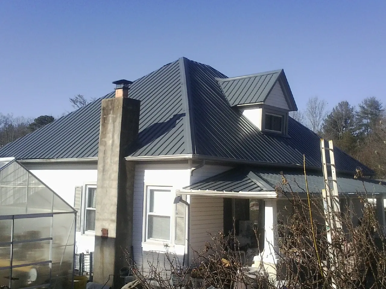 Dark blue standing seam metal roof on a white farmhouse with dormer — Slate & Tile Roof Repair by Roofing Brothers in Castroville