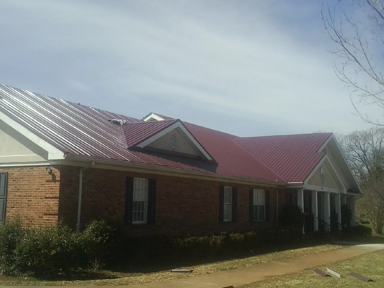 Red metal roof with gabled entries on a long brick building, from a Hail Damage Roof Repair job in Castroville