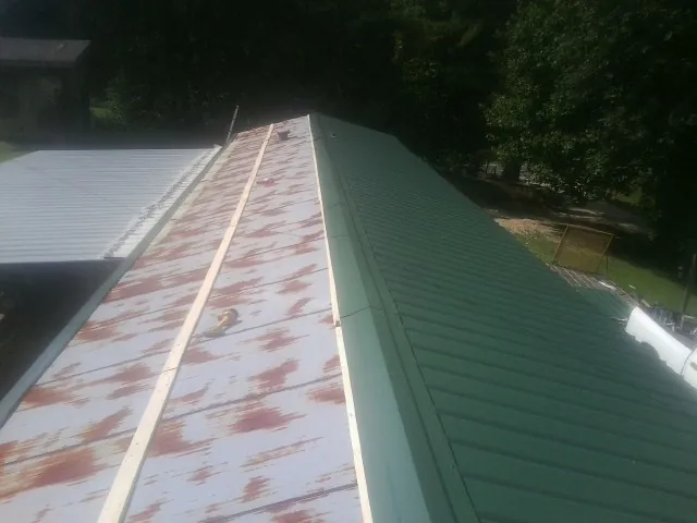 Old rusted panels beside newly installed green metal roofing — Wind Damage Roof Repair by Roofing Brothers in Castroville