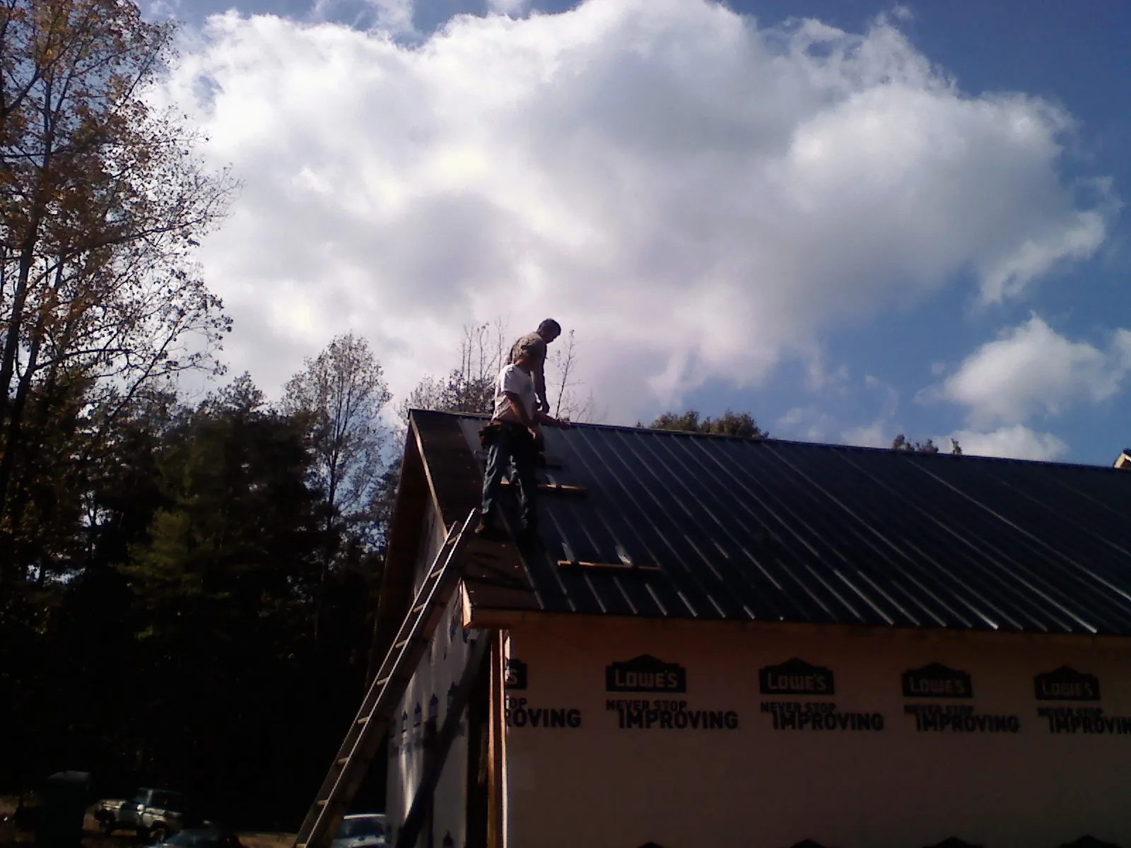 Roofer fastening dark metal panels high against a cloudy sky, from a Roof Inspection job in Castroville